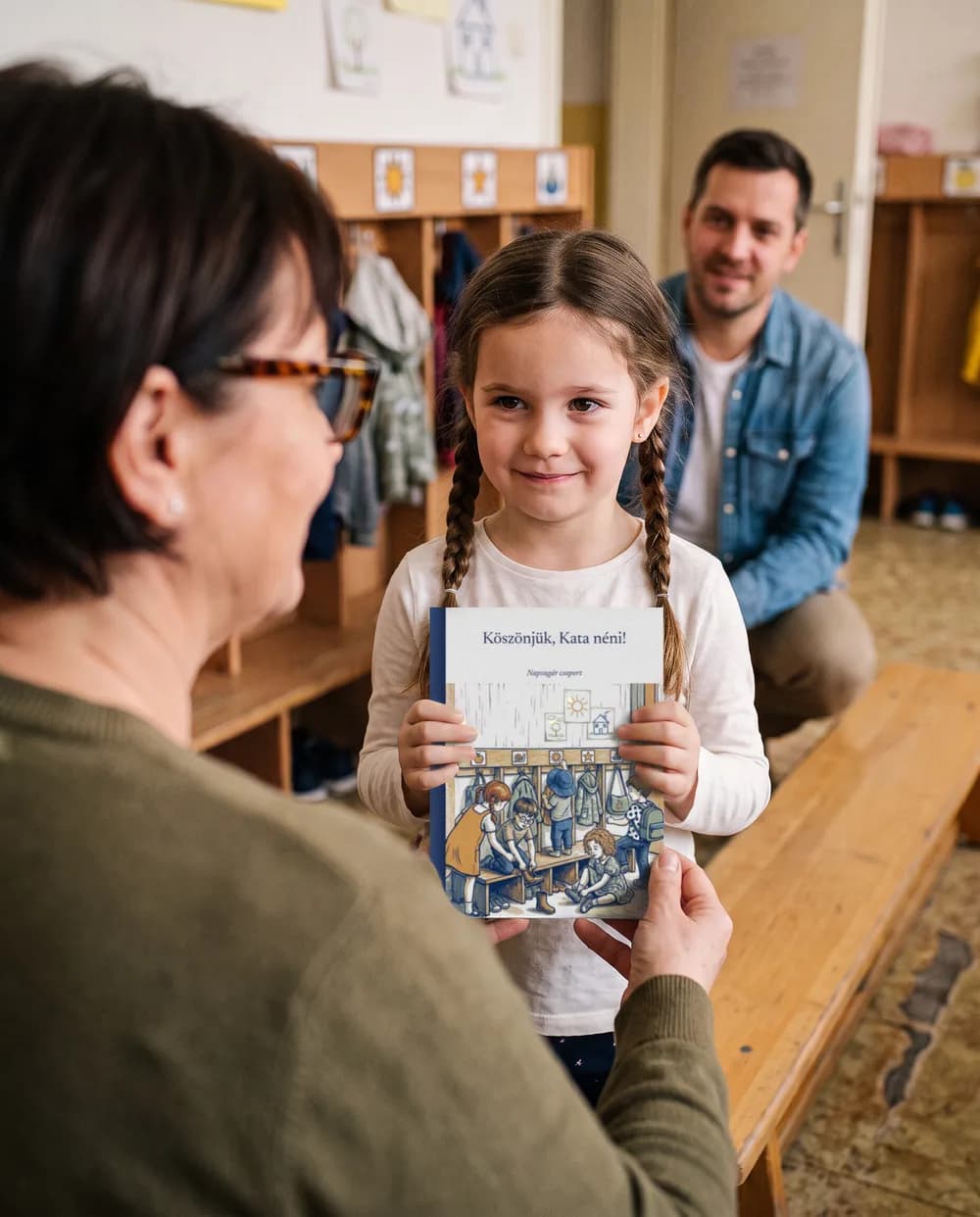 Egy kislány az óvodai öltözőben átadja az óvó néninek a Köszönjük, Kata néni! című könyvet
