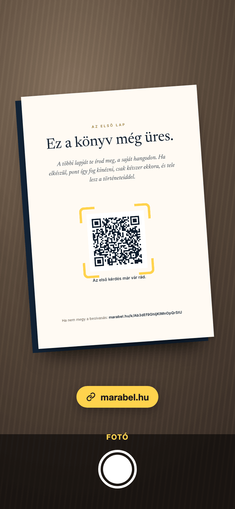 Telefon kamerája a kinyomtatott kártya első lapja fölött: a QR-kód körül keret, alatta a marabel.hu link.